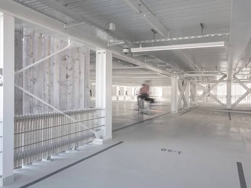 Interior parking level with exposed metal ceiling, white steel bracing and a cyclist in motion blur