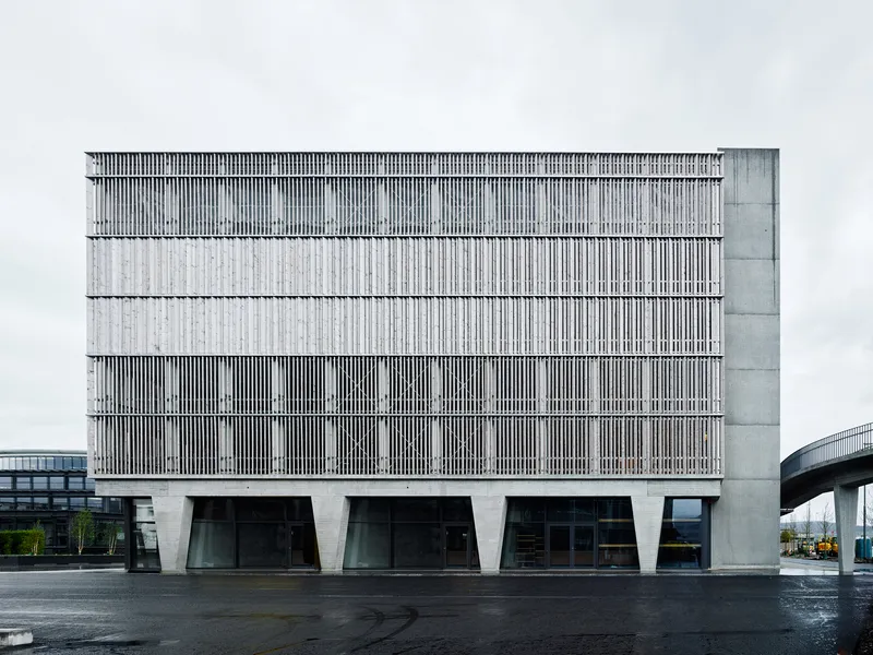 Frontal view of the louvered facade with alternating bands above angled ground floor columns after rainfall