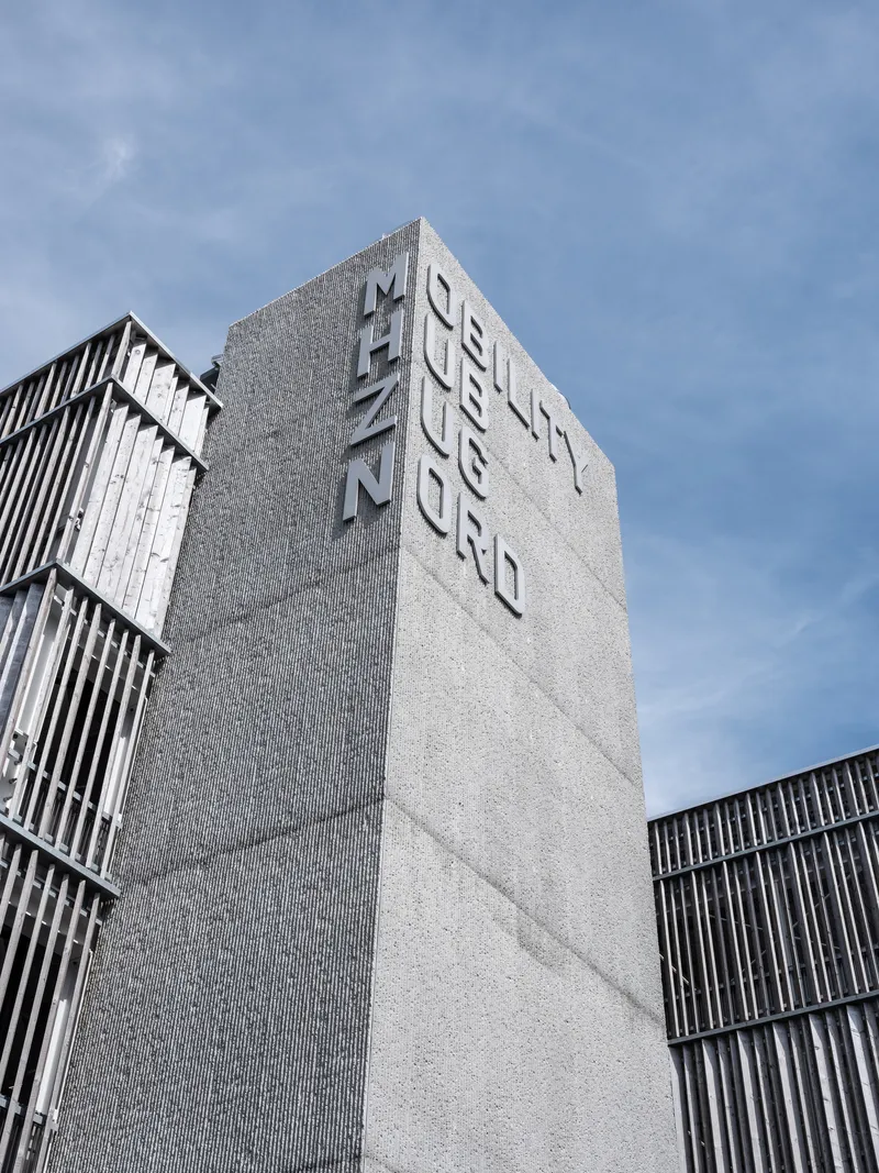 Upward view of the textured concrete tower with raised letterforms against a blue sky