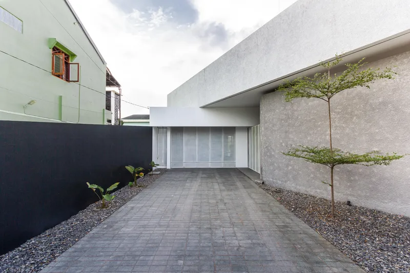 Paved entry drive with a young tree in gravel planting bed beside textured concrete walls