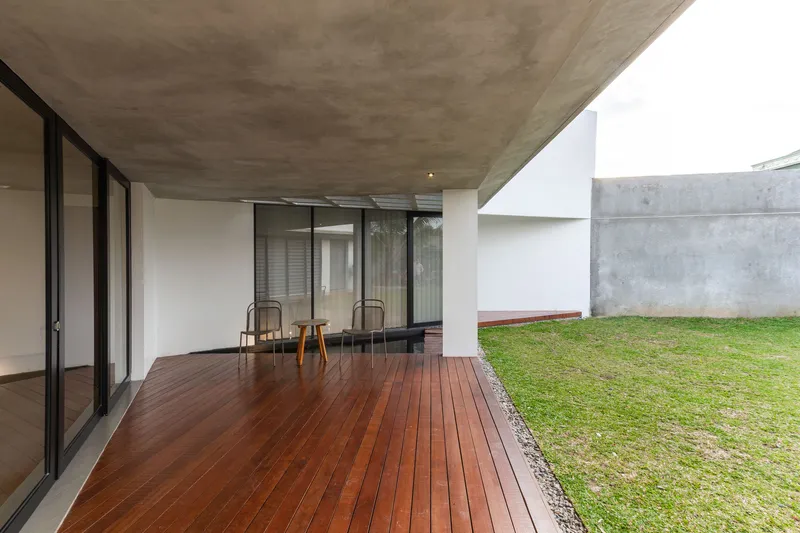 Covered terrace with timber decking and two chairs overlooking a grassed courtyard with concrete walls