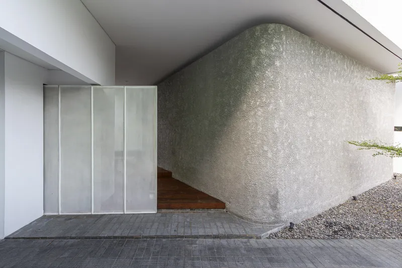 Entry porch corner showing translucent sliding panels meeting textured concrete wall and timber deck edge