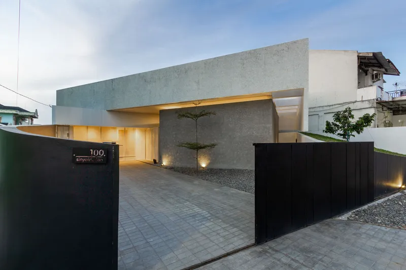 Street view of the concrete entrance with illuminated carport and black metal sliding gate at dusk