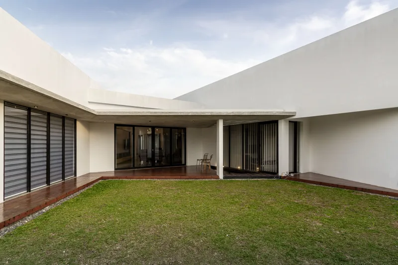 Private courtyard with grass lawn bordered by timber deck and white rendered walls under cloudy sky