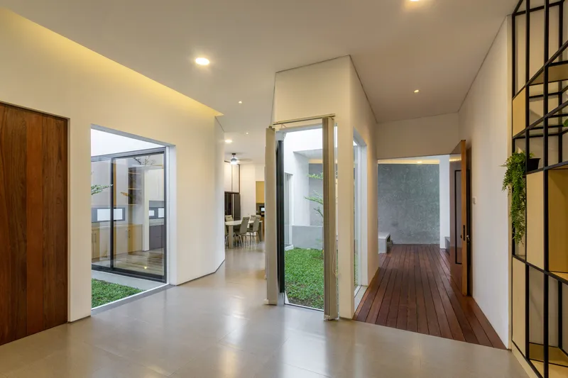 Circulation corridor with glazed courtyard views, spiral stair and timber doors under recessed lighting
