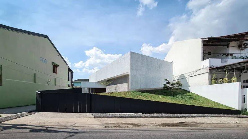 Street view showing a sloped grass lawn rising above a black base wall between neighboring buildings