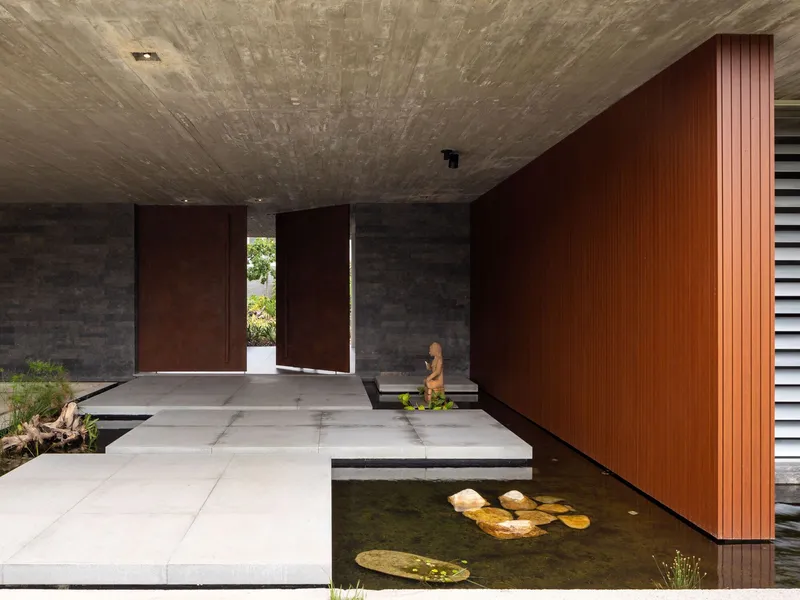 Covered entrance with board-formed concrete ceiling, timber-clad wall, and stepping stones over a reflecting pool