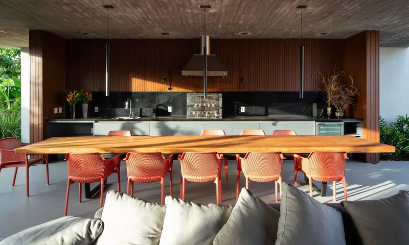 Open-plan kitchen and dining area with timber slatted walls and orange mesh chairs beneath pendant lights