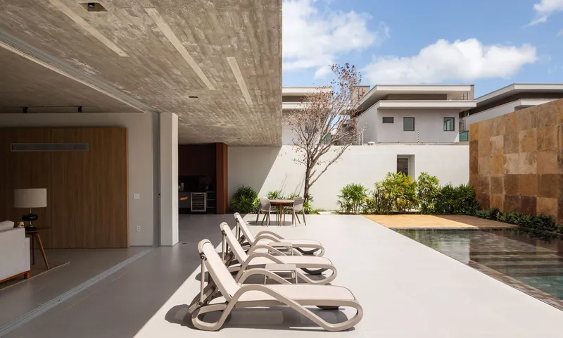 Pool terrace with lounge chairs under a concrete soffit looking toward a courtyard tree in bright daylight