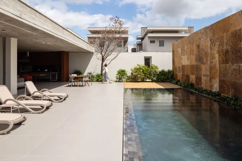 Courtyard pool with large format tile paving bordered by a textured stone wall and leafless tree