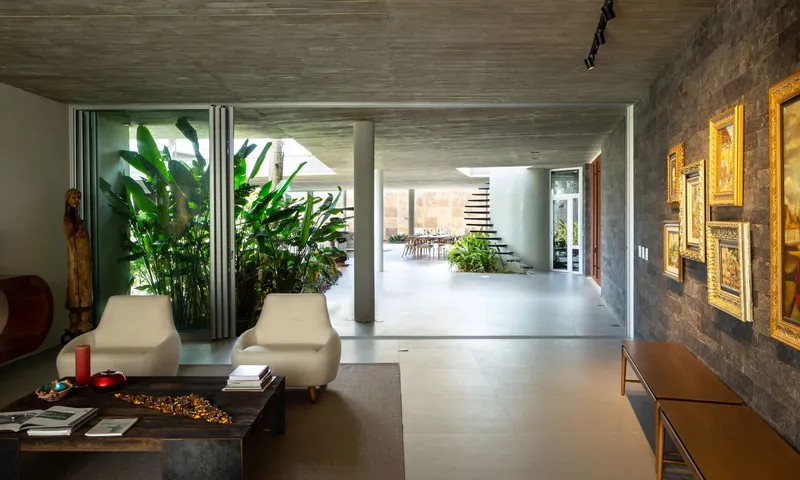Living room view through to interior courtyard planted with tall banana palms under exposed concrete ceiling
