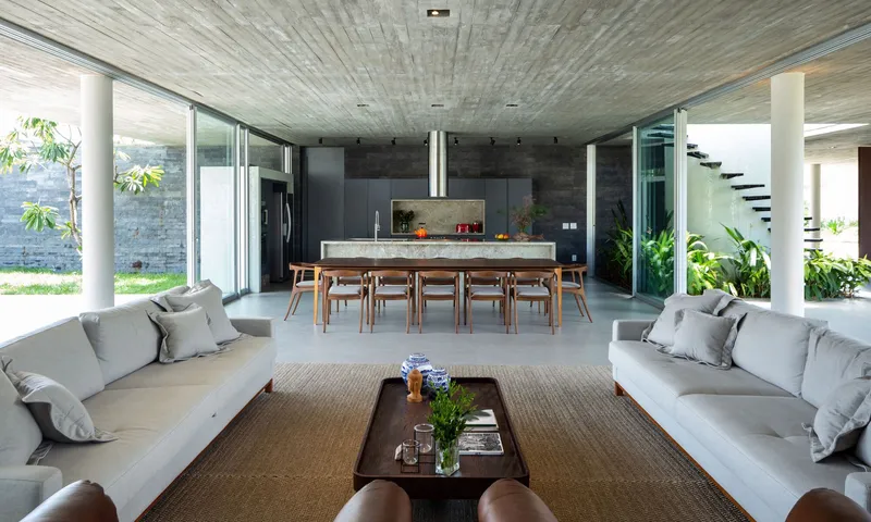 Open-plan living and dining space with board-formed concrete ceiling and view to planted courtyard beyond