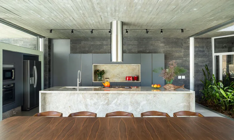 Kitchen island with veined marble counter and suspended cylindrical steel hood beneath board-formed concrete ceiling