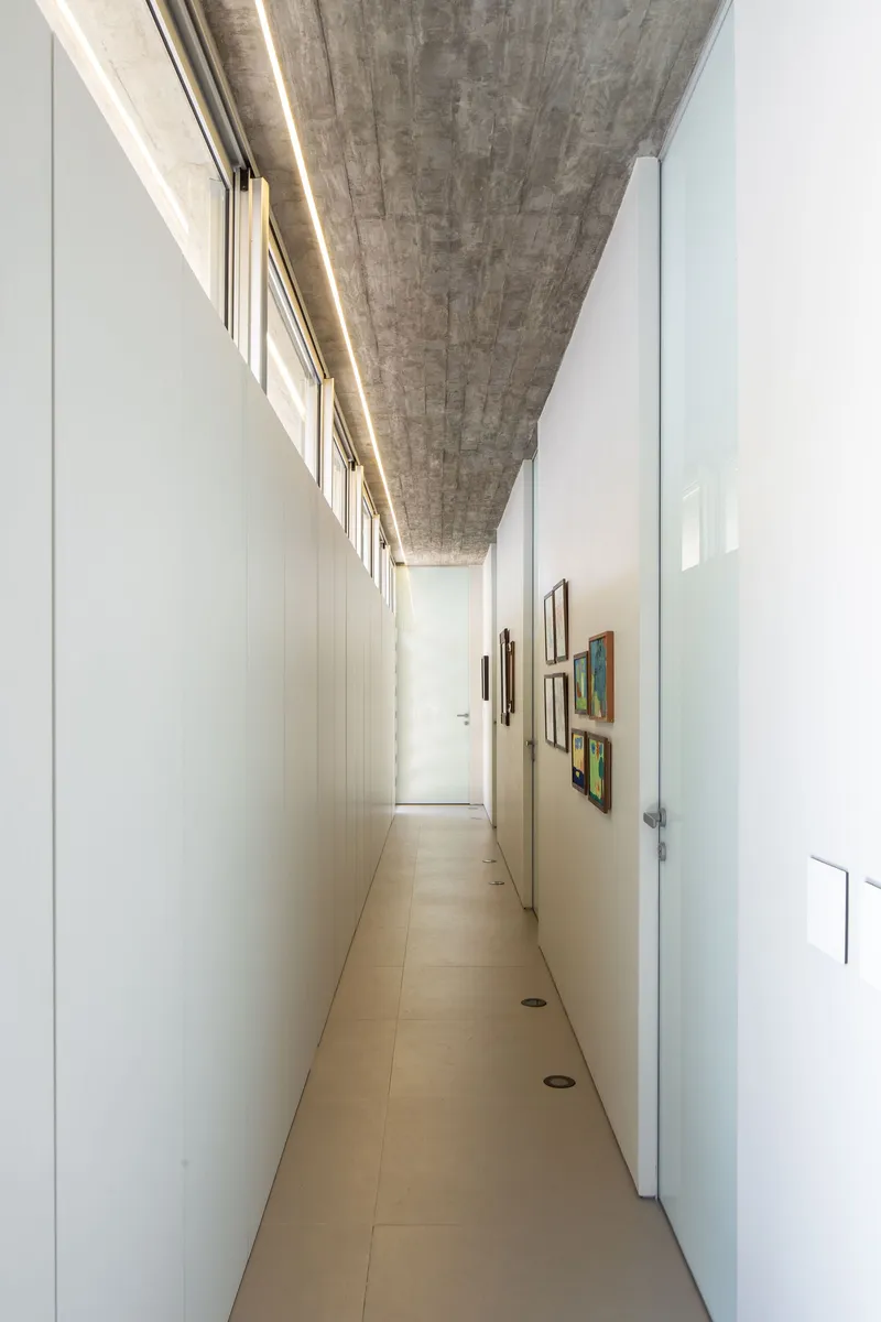 Corridor with exposed board-formed concrete ceiling, white walls, and linear skylight along one edge