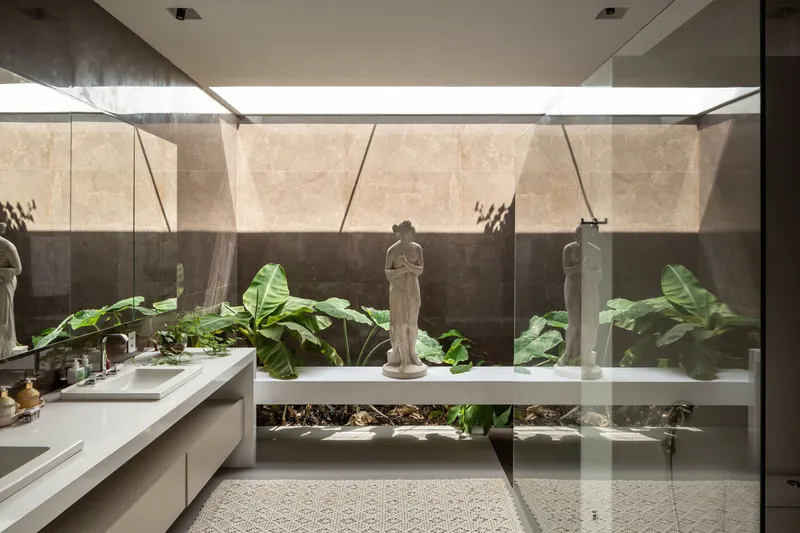 Bathroom with stone-clad wall, integrated planter bed of tropical foliage, and sculpture behind glass partition