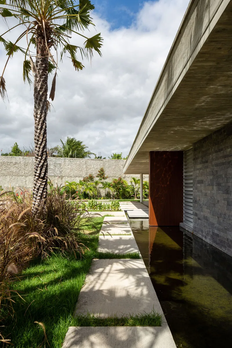 Covered walkway with concrete soffit alongside planted beds with palm trees and grasses under cloudy skies