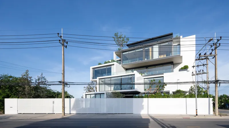 Street elevation showing the layered white facade behind overhead power lines and perimeter wall