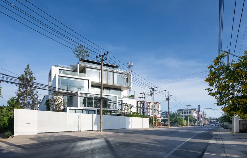 Street view of white stacked volumes with full-height glazing beneath clear blue sky and overhead power lines