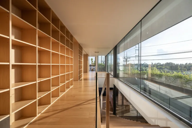 Upper-level corridor with floor-to-ceiling timber shelving along one wall and glazed balustrade overlooking planted terrace below