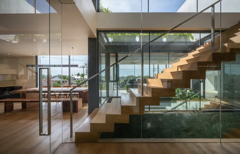 Interior view of timber staircase with glass railings rising through a double-height space lit by skylights