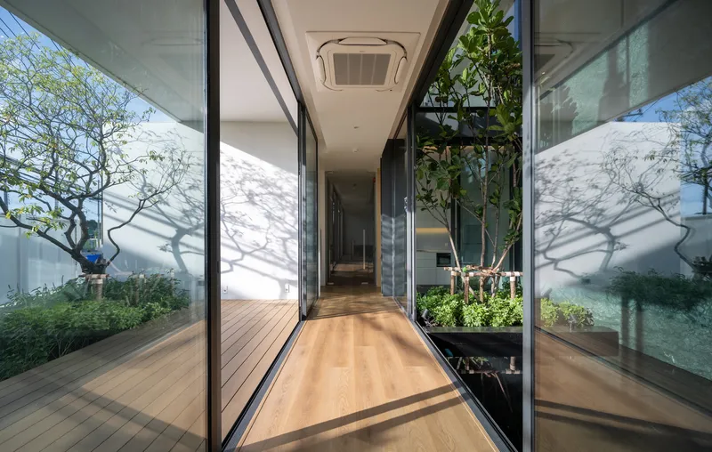Corridor with sliding glass walls flanking a central planted courtyard with dappled shadows