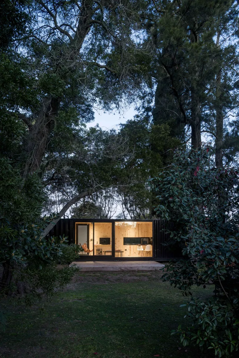 Timber deck extending from the glazed facade of a black-clad structure at twilight
