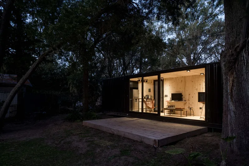Corner view of the plywood-lined interior visible through floor-to-ceiling glass at dusk