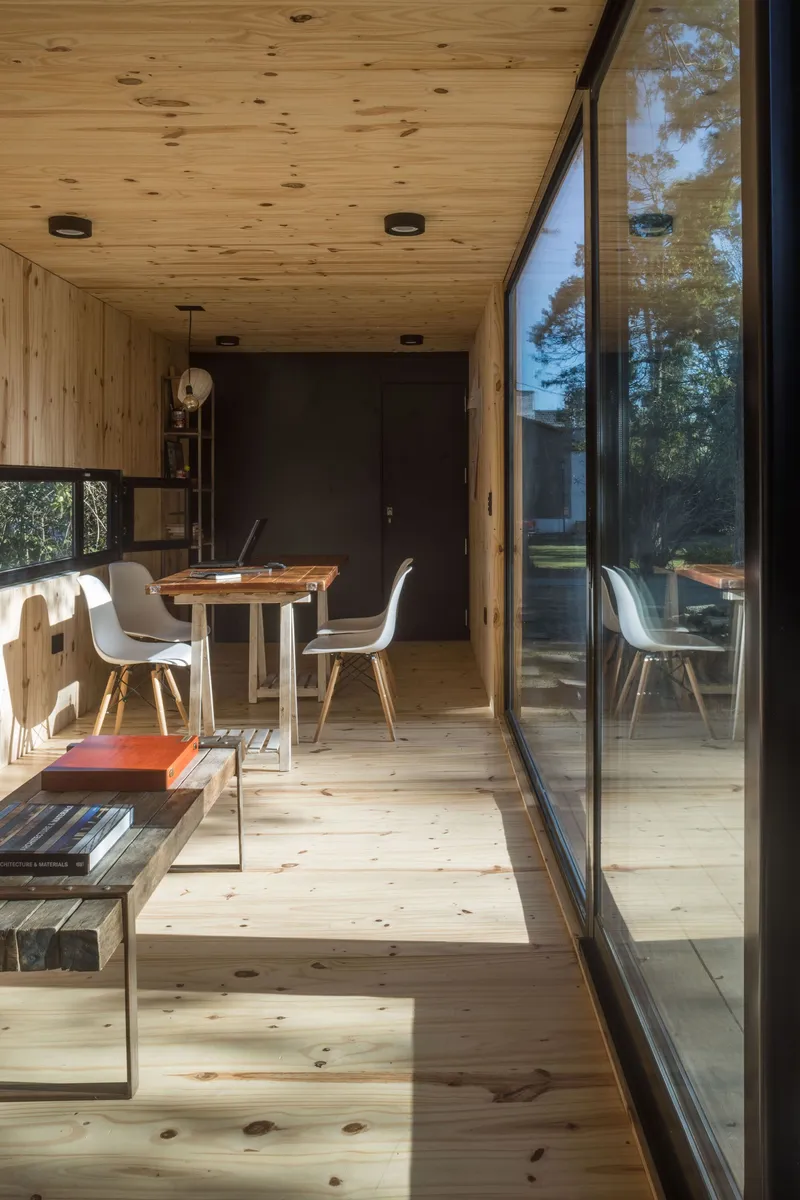 Pine-lined dining space with sunlight streaming through floor-to-ceiling glass onto the timber floor