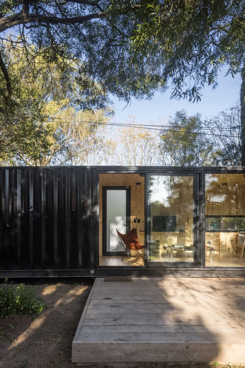 Entrance with plywood door and floor-to-ceiling glass framed by vertical corrugated metal cladding