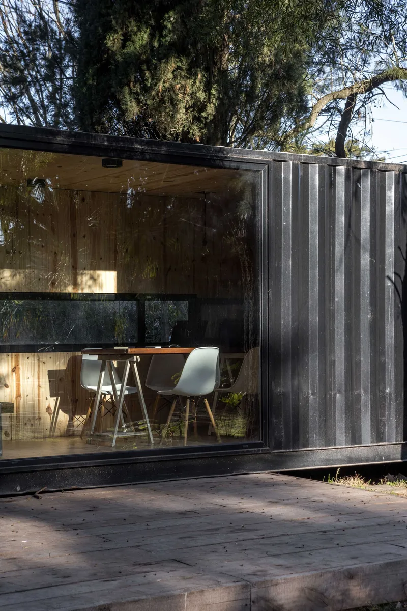 Corner detail showing corrugated metal cladding meeting full-height glass with dining furniture visible inside