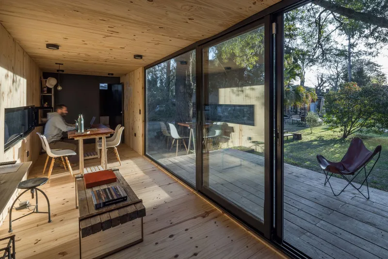 Interior dining area with timber ceiling and floor opening onto a wooden deck through sliding glass doors