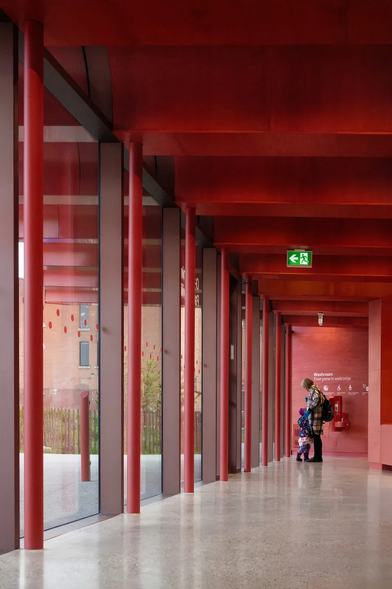 Interior corridor with red steel columns and red-painted ceiling beams with a figure walking