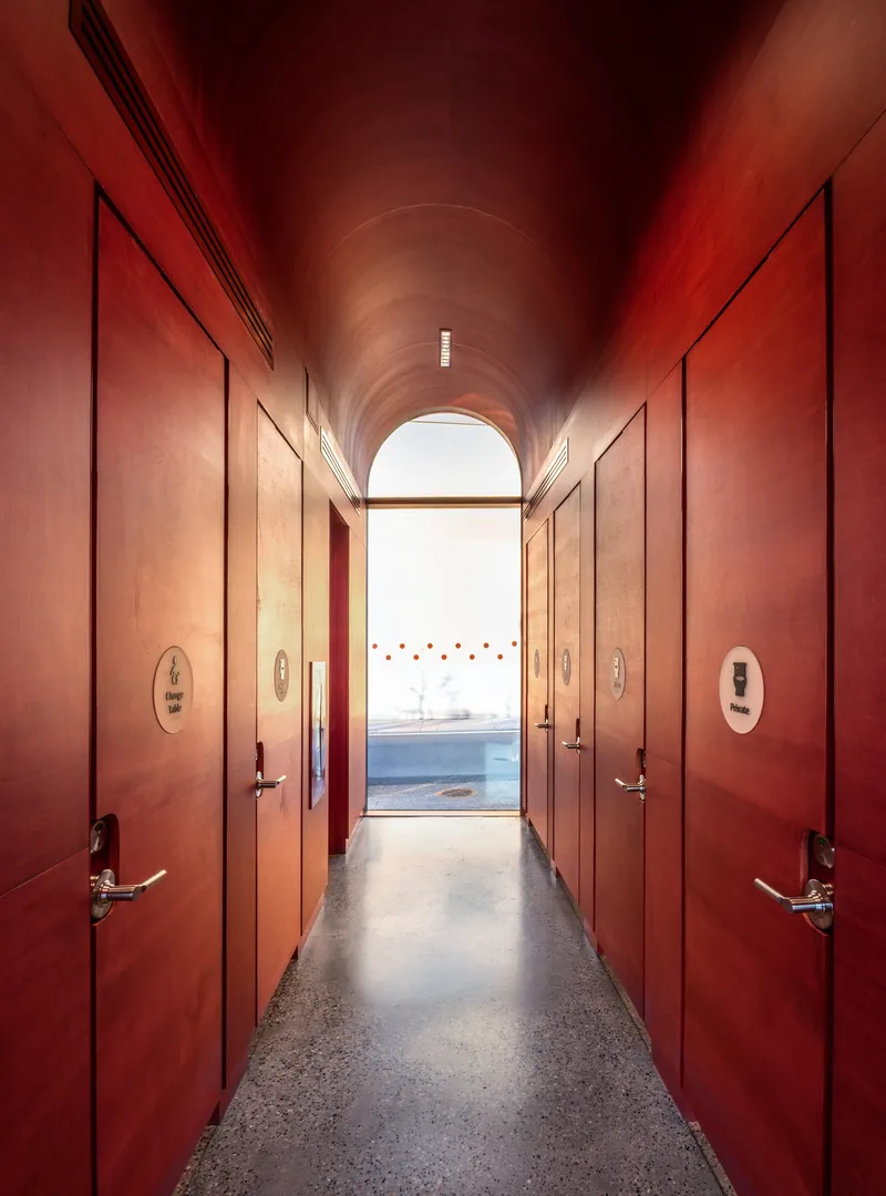 Vaulted corridor with red plaster walls and terrazzo flooring leading to an arched opening