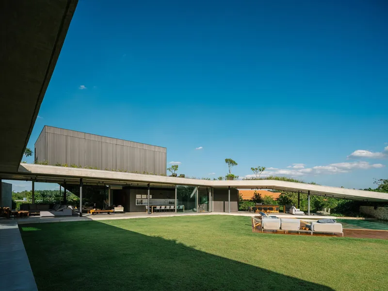Grass courtyard framed by covered pavilions with planted roofs under a clear blue sky