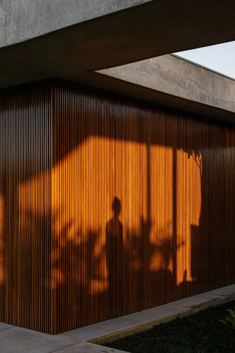 Vertical timber screen wall with silhouettes of interior figures illuminated by warm light at dusk