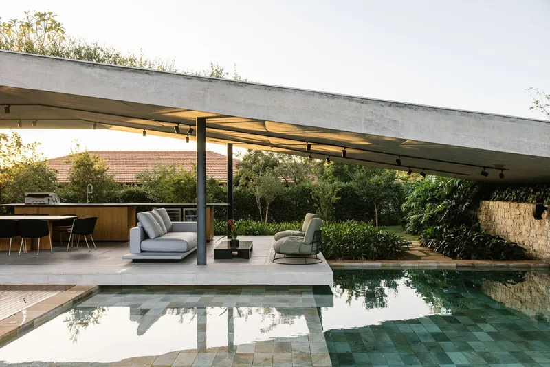 Pool deck and covered pavilion reflected in still water with planted roof garden beyond