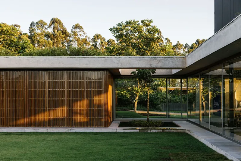 Slatted timber volume with concrete beam beside glass walls enclosing an interior courtyard garden