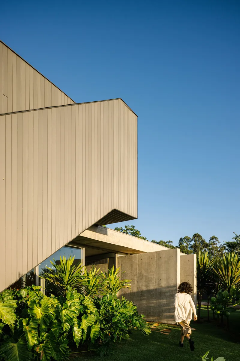Cantilevered timber volume over concrete base with a figure walking through the planted lawn