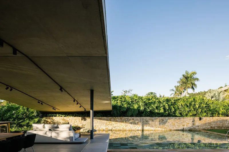 Covered pool terrace with exposed concrete soffit and limestone retaining wall beyond the water
