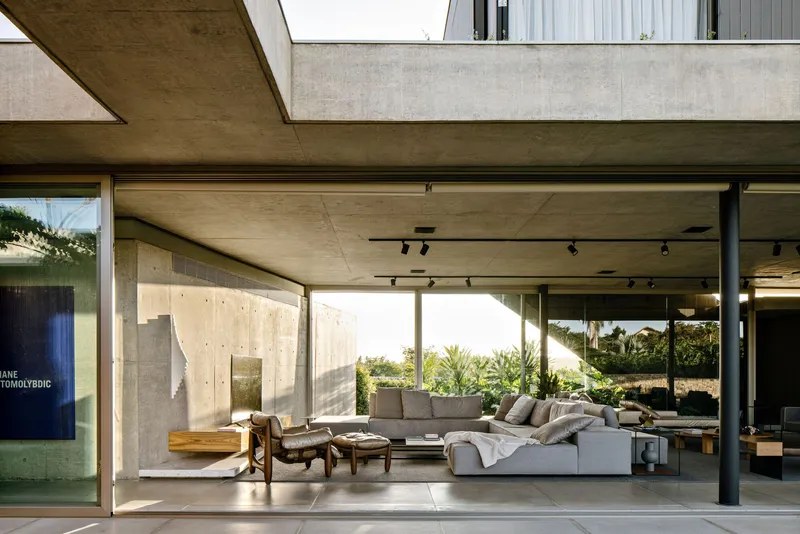 Covered terrace with concrete ceiling and columns opening to a sunlit courtyard beyond the seating area