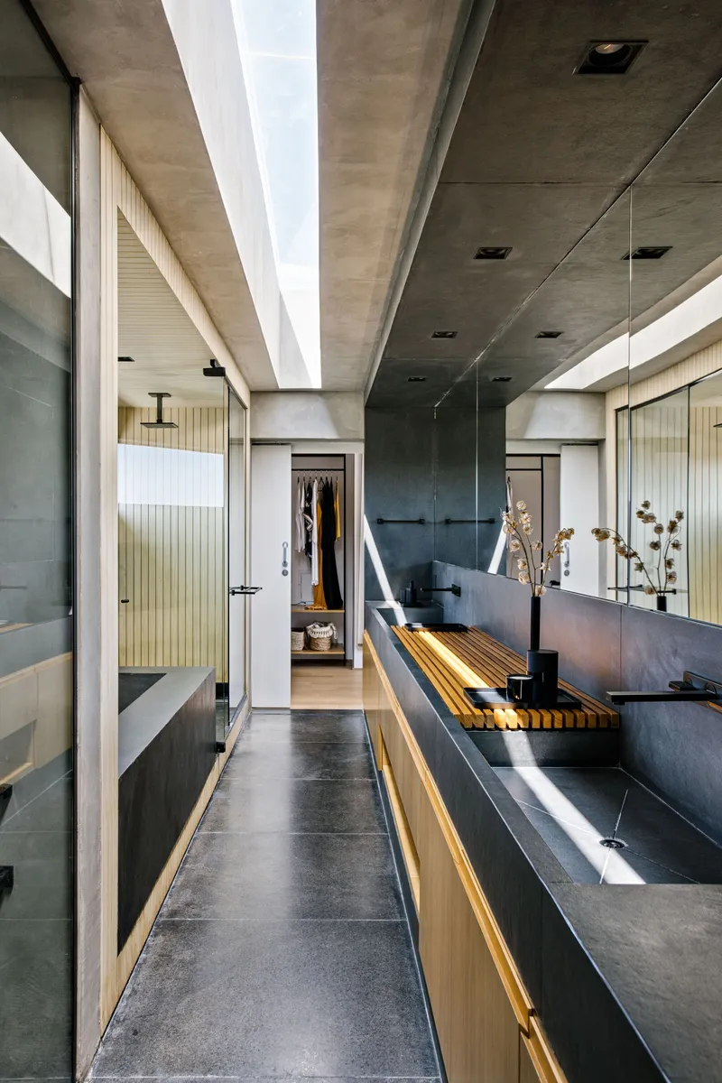 Bathroom with slatted timber bench and concrete vanity under a skylit ceiling opening