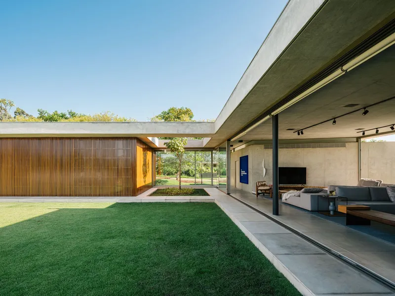 Courtyard edge showing timber wall volume meeting concrete terrace with interior visible through open glazing