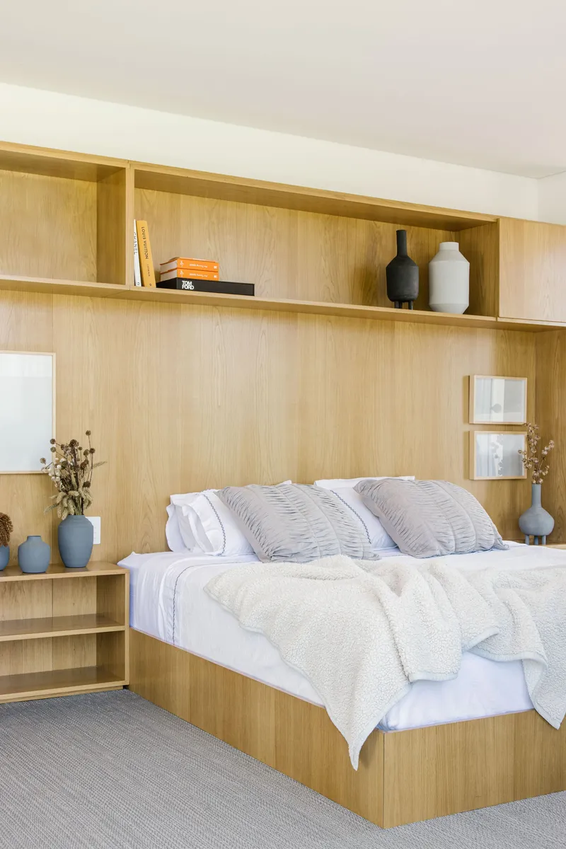 Built-in blonde wood bed platform with integrated shelving and overhead storage niches