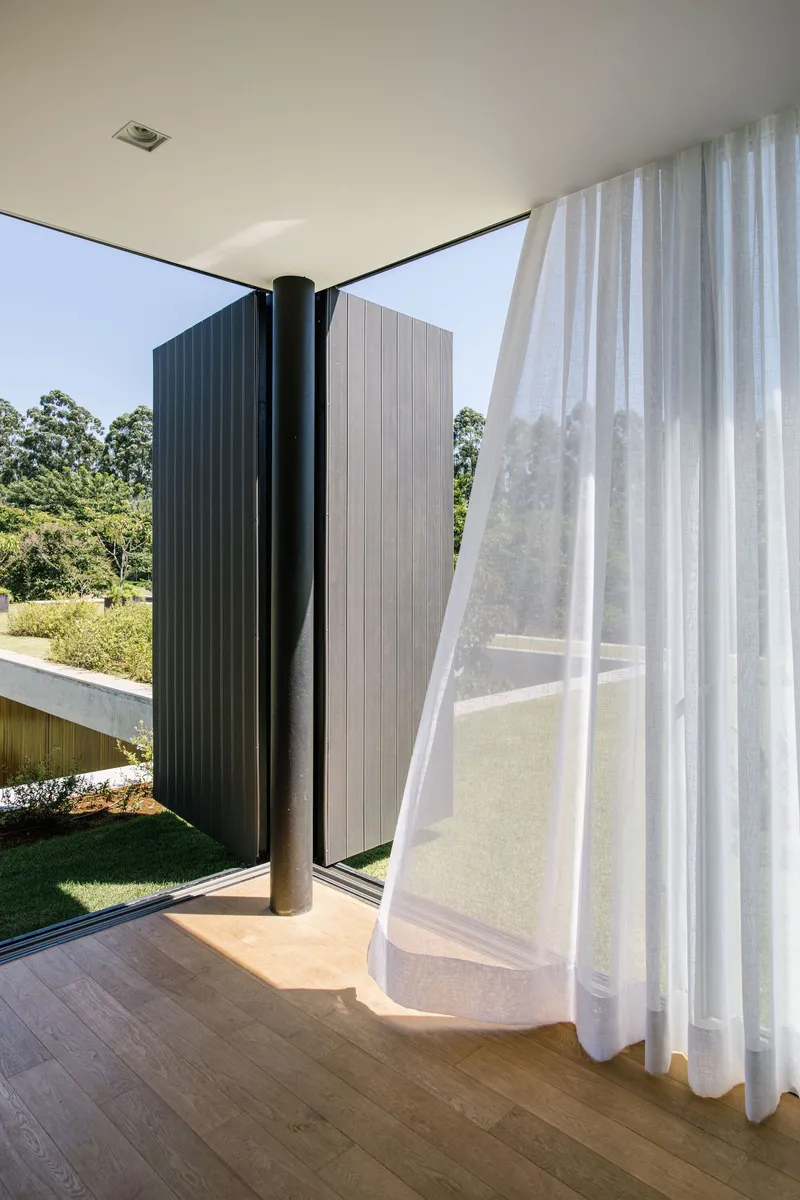 Corner glazing with black pivot door and sheer curtain billowing in sunlight