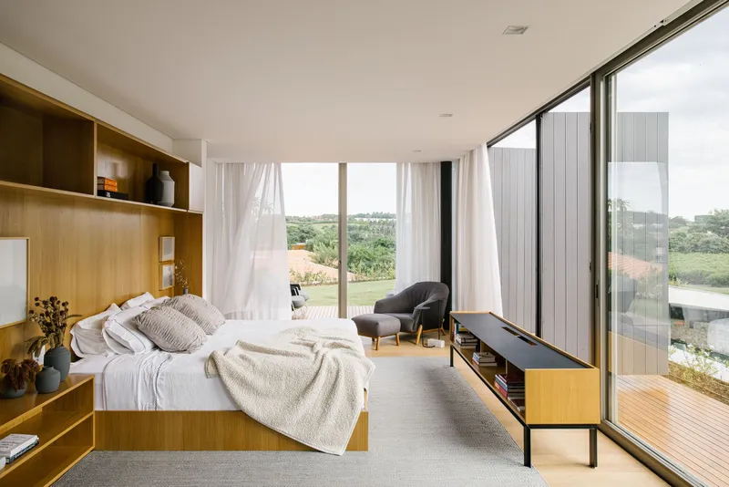 Bedroom with integrated timber storage headboard and floor-to-ceiling glazing overlooking the landscape