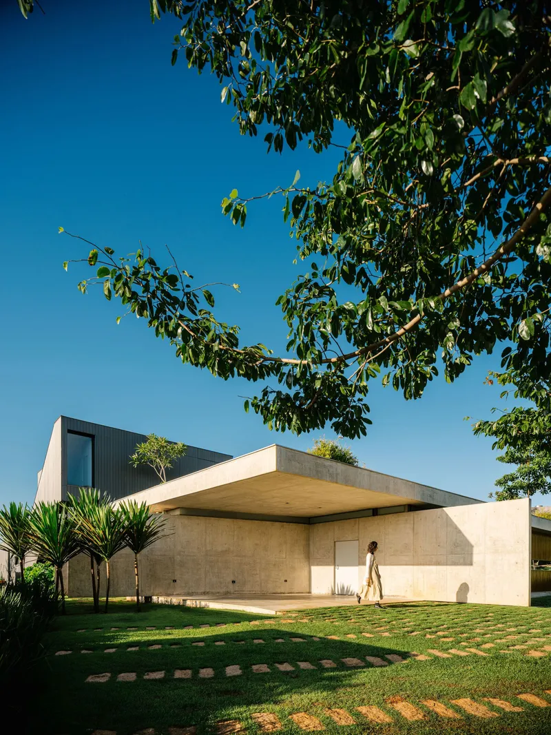 Board-formed concrete wall with recessed door as a figure walks across the lawn in shadow