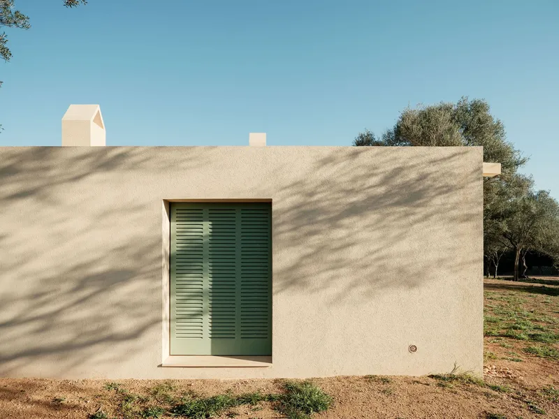 Exterior wall with recessed window fitted with green timber shutters among olive trees