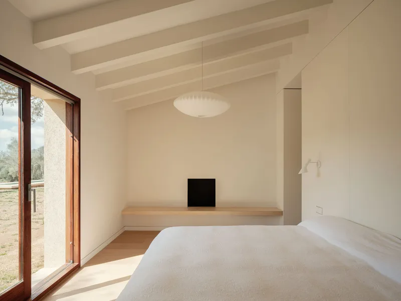 Bedroom with exposed timber beams, pendant light, and glazed door opening to olive grove