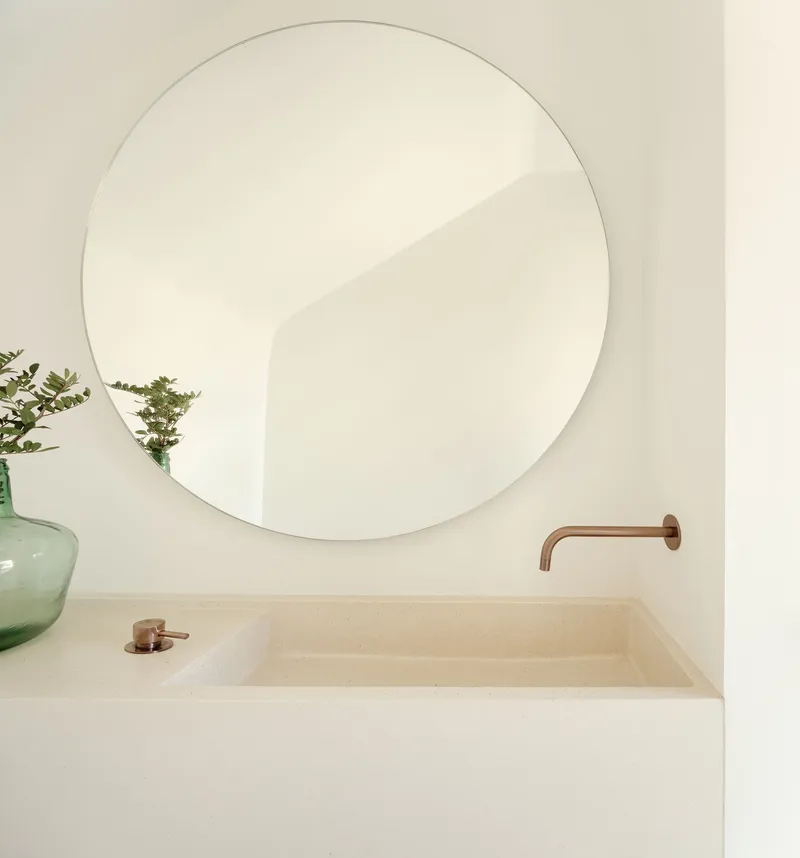 Bathroom vanity with integrated stone basin, round mirror, copper faucet, and glass vase