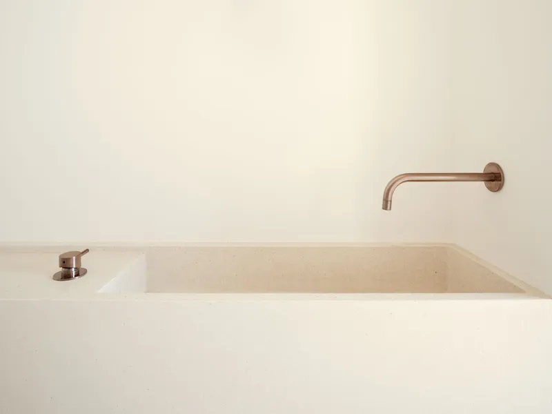Close-up of the rectangular stone basin with wall-mounted copper faucet and soap dispenser